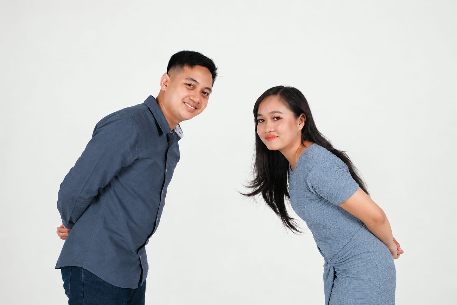 Kristinne and Carlo leaning towards each other in front of a white studio wall, both in blue.