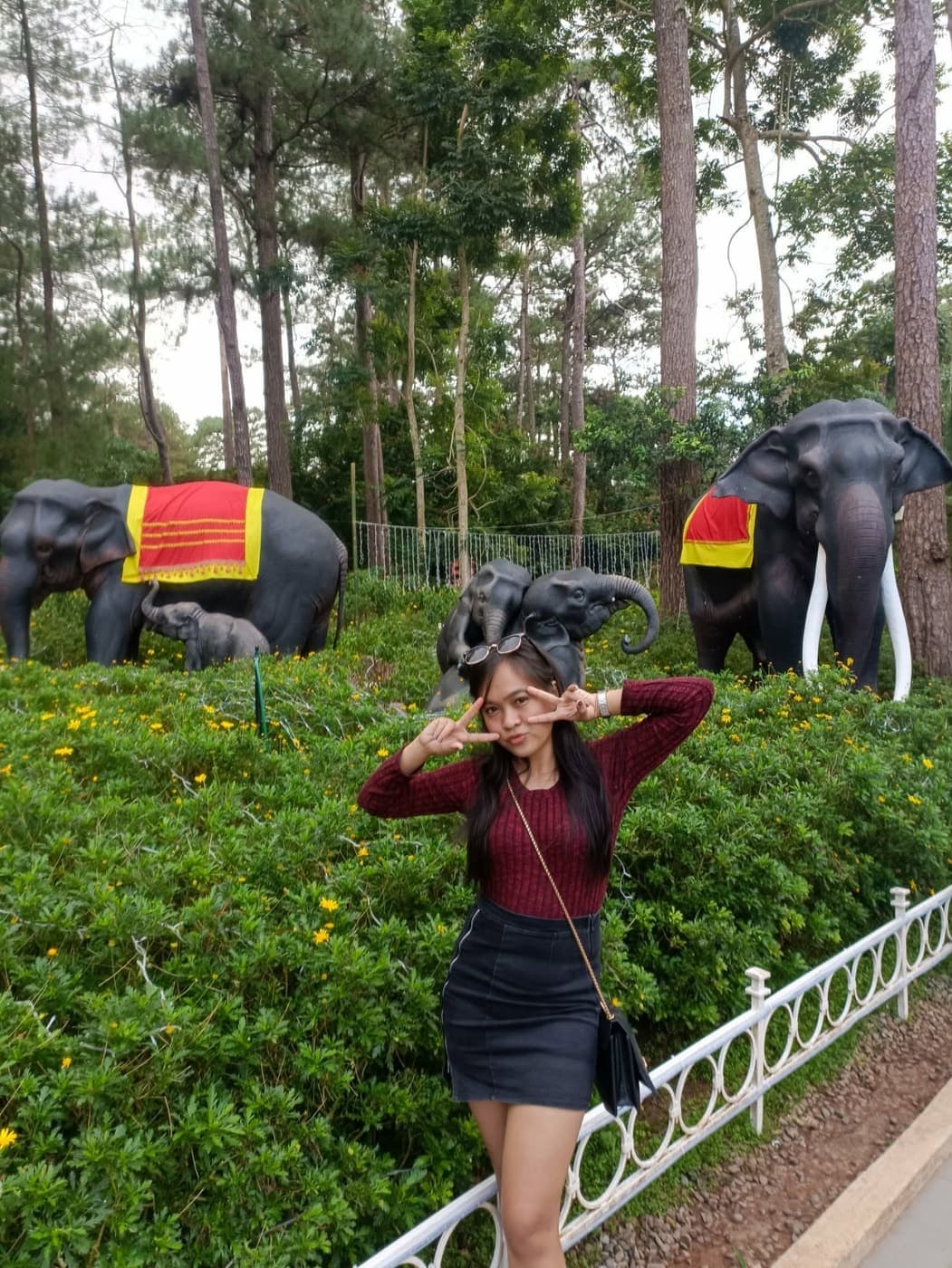 Kristinne making a peace sign in a garden with elephant statues behind her.