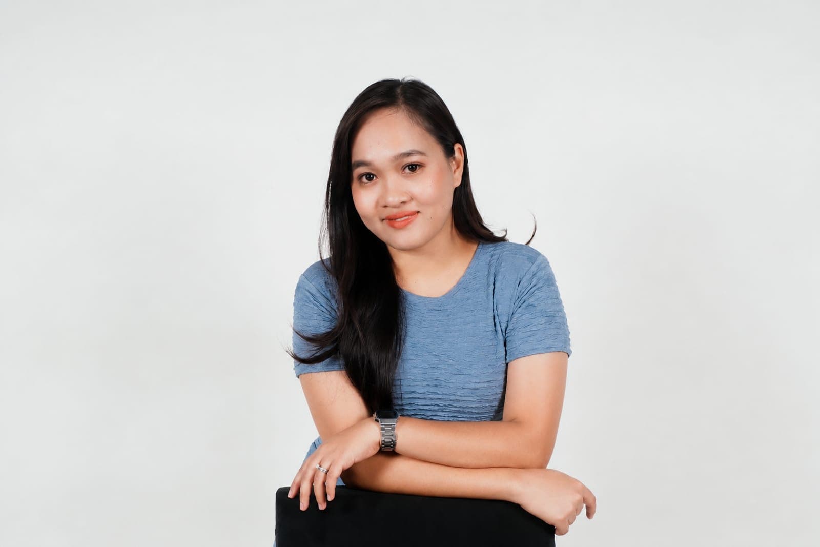 Kristinne leaning on the back of a chair, smiling, in front of a white studio wall.